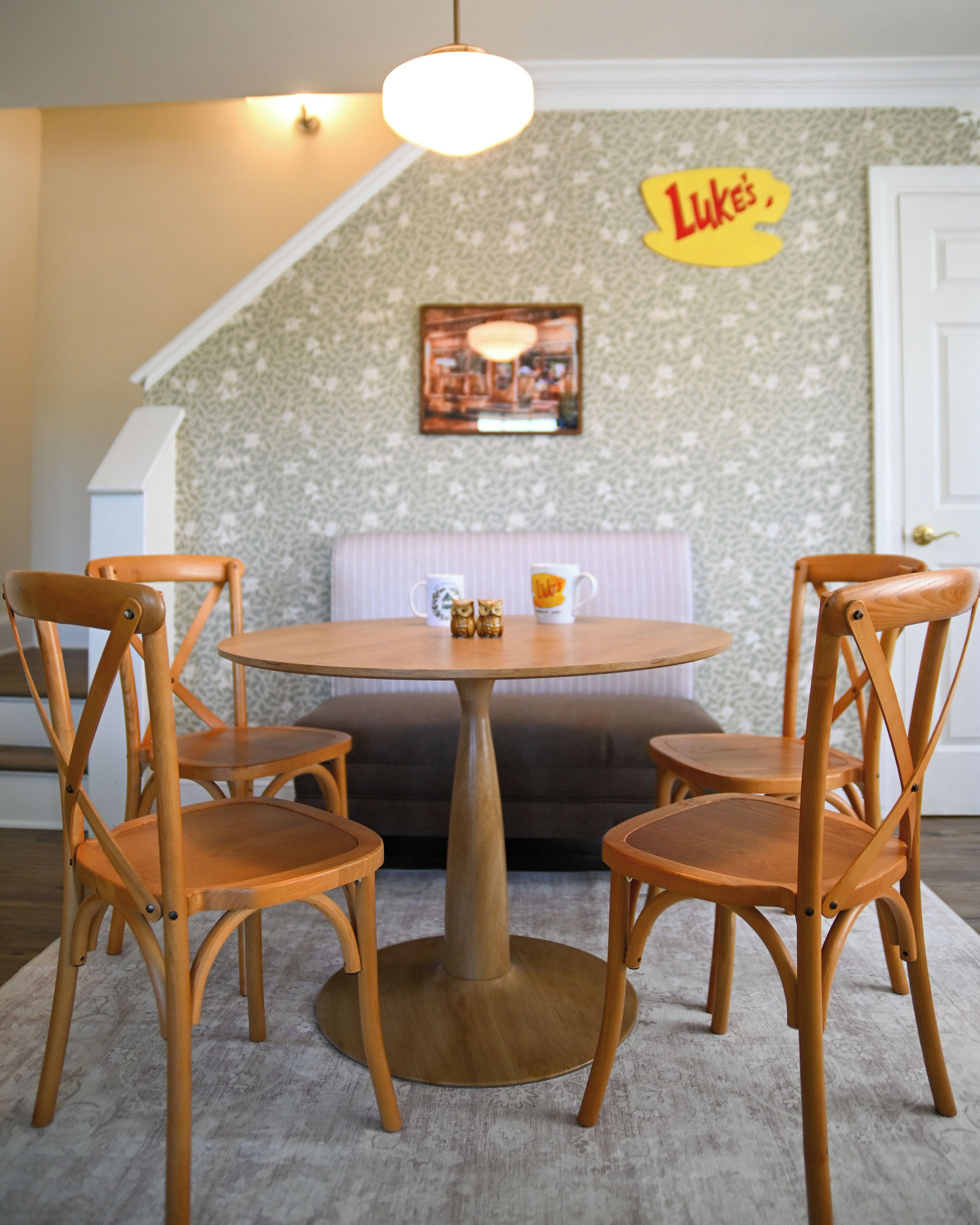 A dining area with a round wooden table, four wooden chairs, a cushioned bench, and a wall-mounted sign.