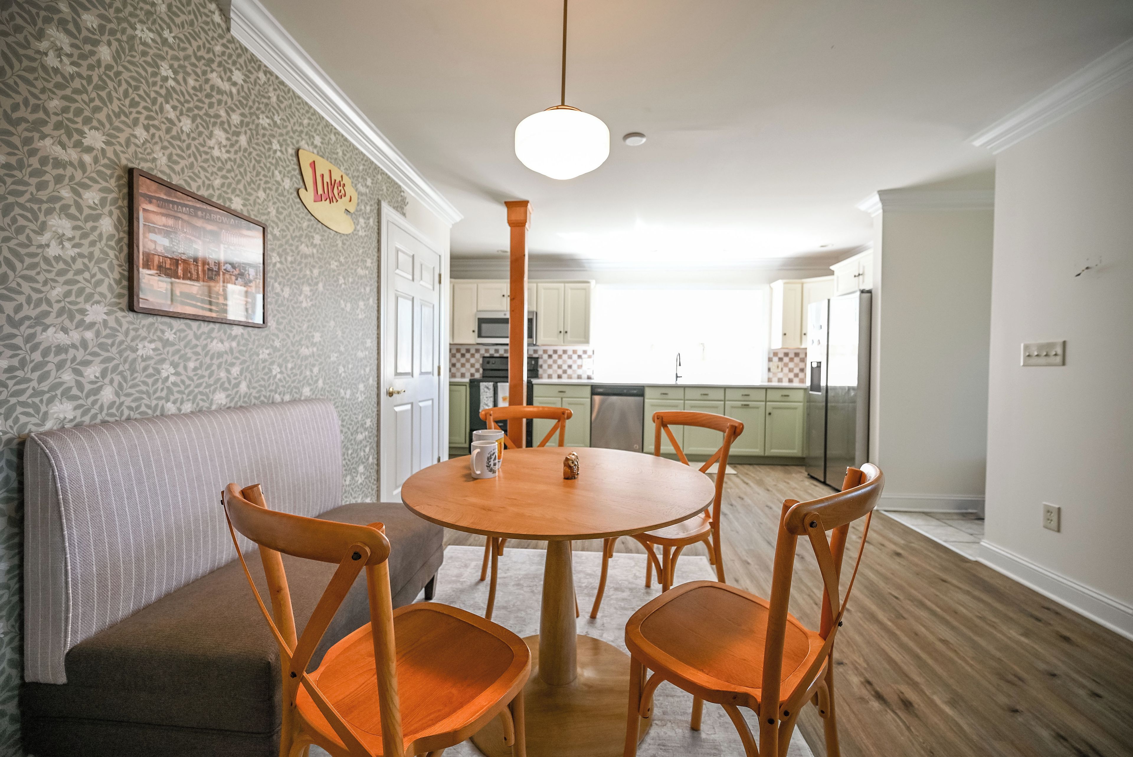 A dining area with a round wooden table, four wooden chairs, a grey sofa, and a kitchen in the background.