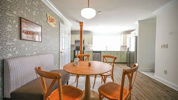 A dining area with a round wooden table, four wooden chairs, a grey sofa, and a kitchen in the background.
