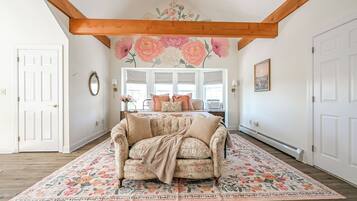 Una habitación con un sofá estampado con motivos florales, un ventanal con persianas, una viga de techo de madera y un mural floral en la pared.