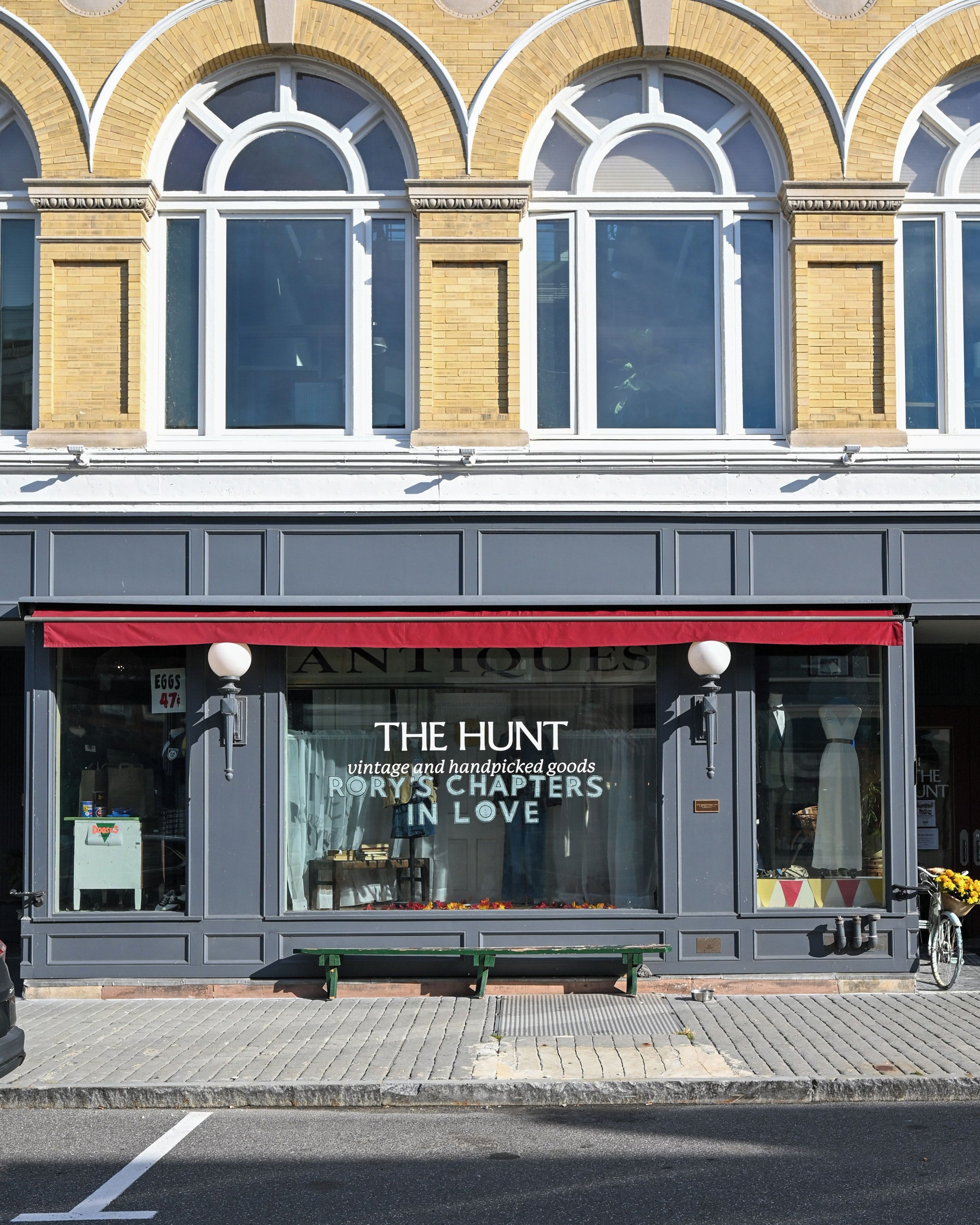Une devanture de magasin avec un auvent rouge et une grande vitrine où sont exposés des articles anciens.