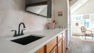 A kitchen with a white countertop, a black sink, wooden cabinets, and a mounted television.