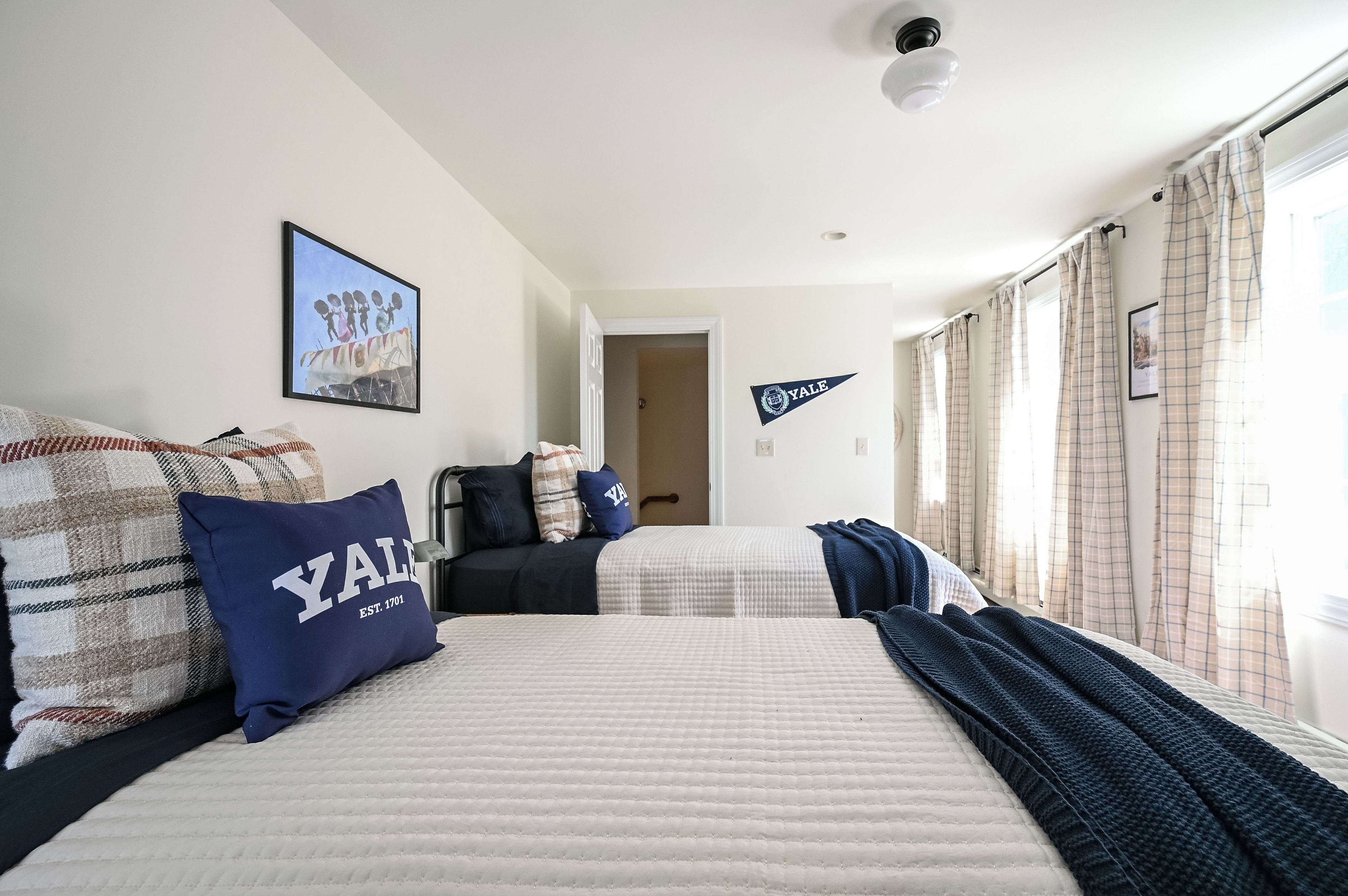 A hotel room with two beds, a framed picture on the wall, and a Yale pennant.