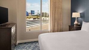 Une chambre d’hôtel avec un grand lit, une table de chevet avec une lampe, une commode et une fenêtre donnant sur le paysage urbain.