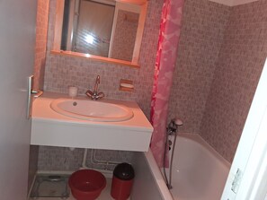 Ein Badezimmer mit einem weißen Waschbecken, einem Spiegel, einem roten Eimer und einer Duschkabine.
