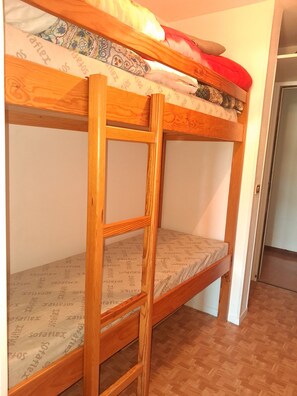 Ein Etagenbett mit einer Holzleiter, einer gemusterten Matratze und einer Tür im Hintergrund.