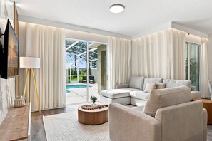 A modern living room with a sectional sofa, a coffee table, and a TV mounted on the wall. - Chic Disney Escape, Themed Rooms & Private Pool (Four Corners)