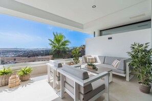 A modern balcony with a sofa, a table, and potted plants. - Mirador Estepona Hills 25 | Pool & Gym | Sea View (Estepona)