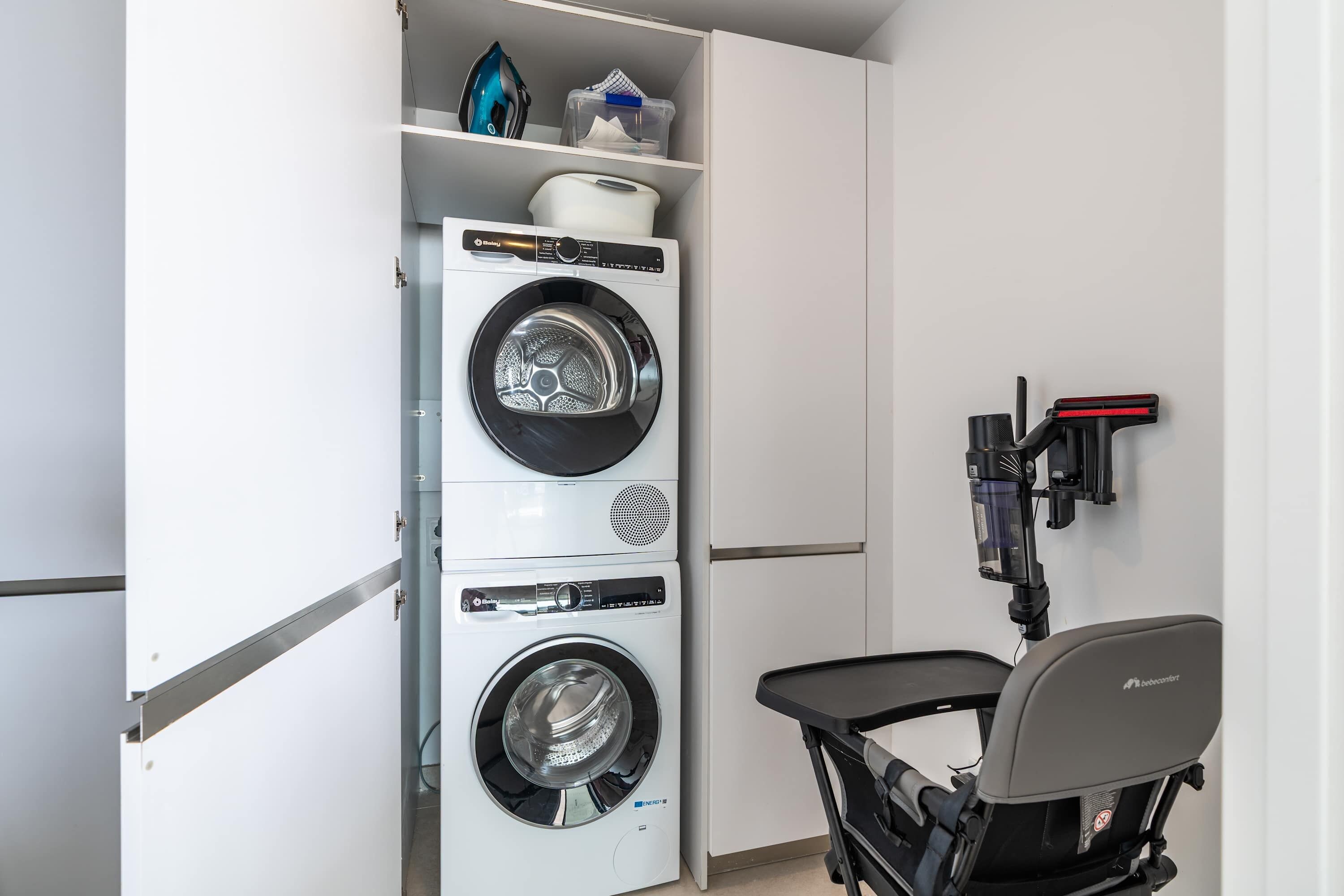 A compact laundry room with a front-loading washer and dryer, a small table, and a wall-mounted ironing board.