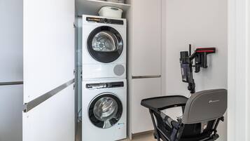 A compact laundry room with a front-loading washer and dryer, a small table, and a wall-mounted ironing board.