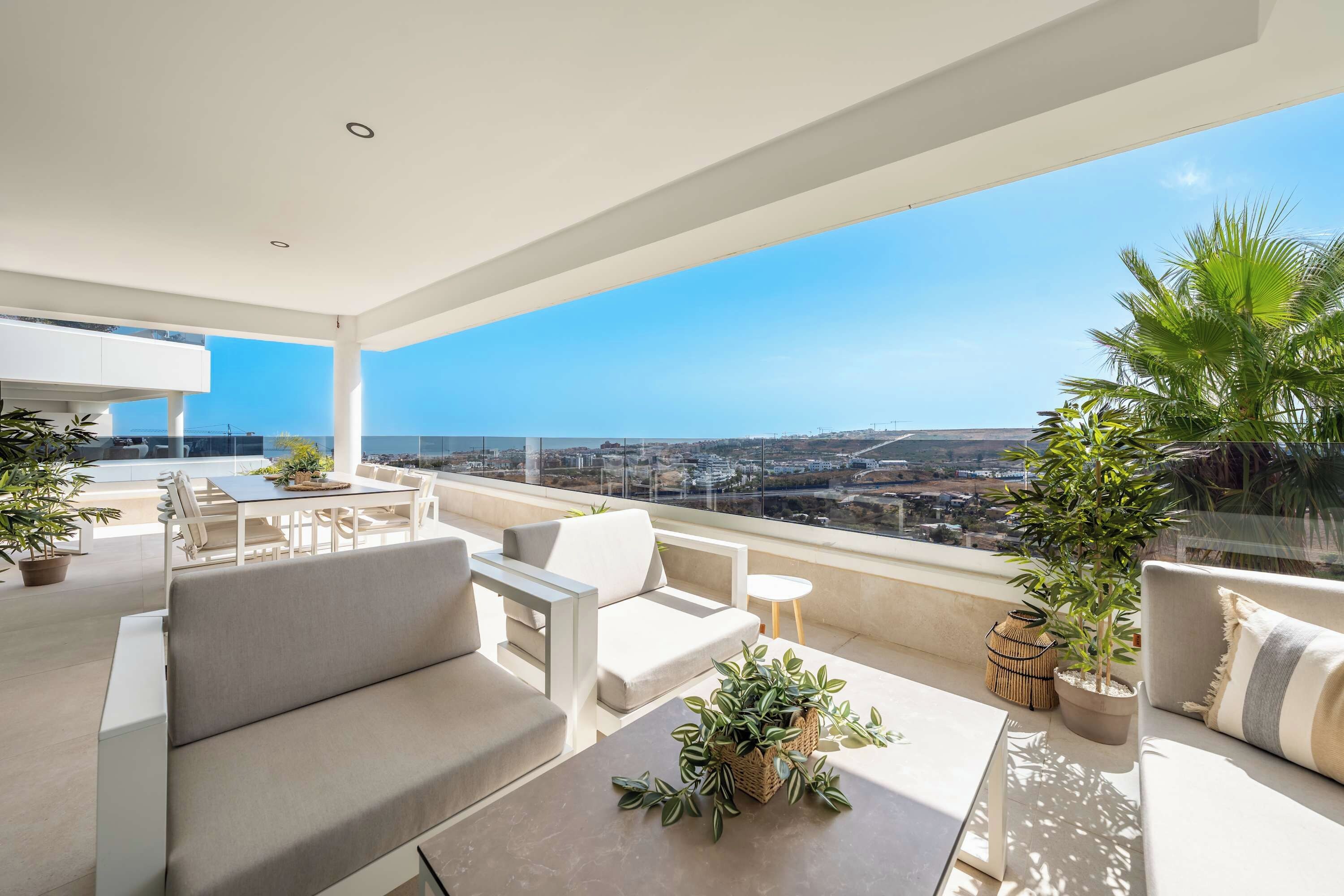 A modern outdoor living space with a sofa, dining table, and chairs, overlooking a cityscape.