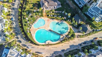 An aerial view of a resort with multiple swimming pools, a bridge, and surrounding greenery.