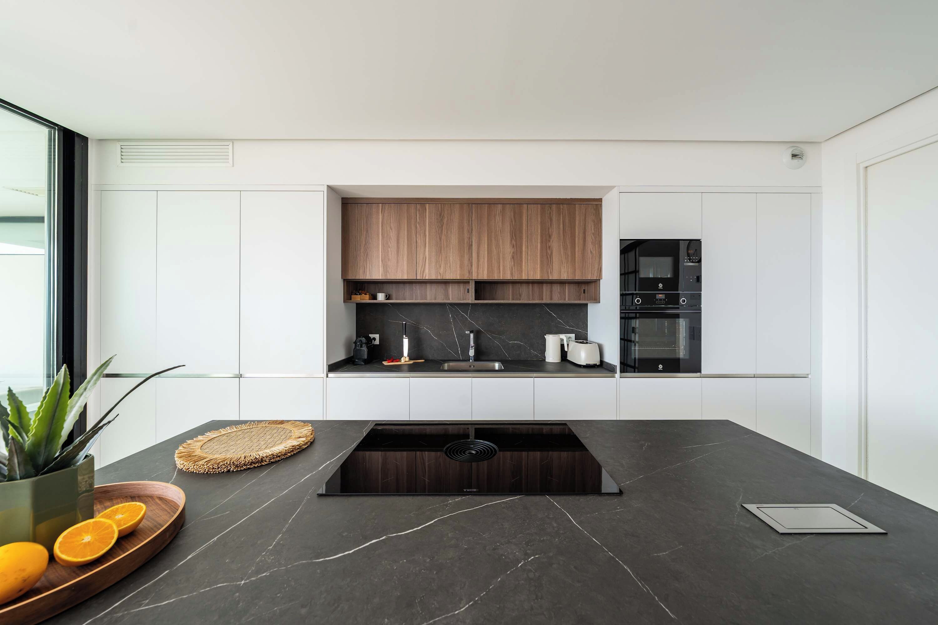 A modern kitchen with a dark countertop, wooden cabinets, and a built-in oven.