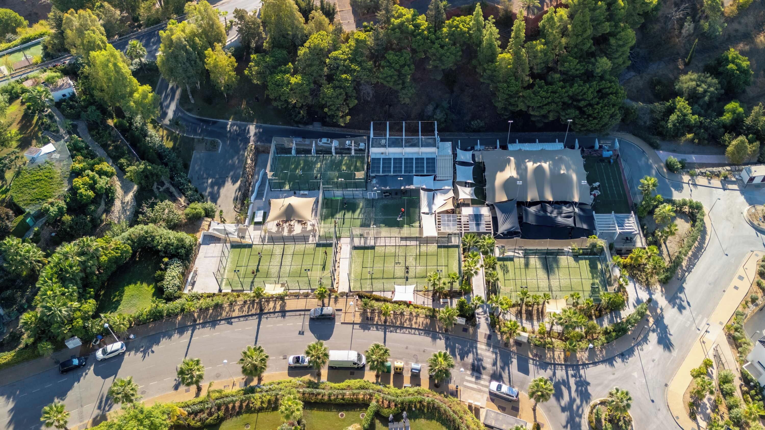 An aerial view of a property with multiple tennis courts, a parking area, and surrounding greenery.