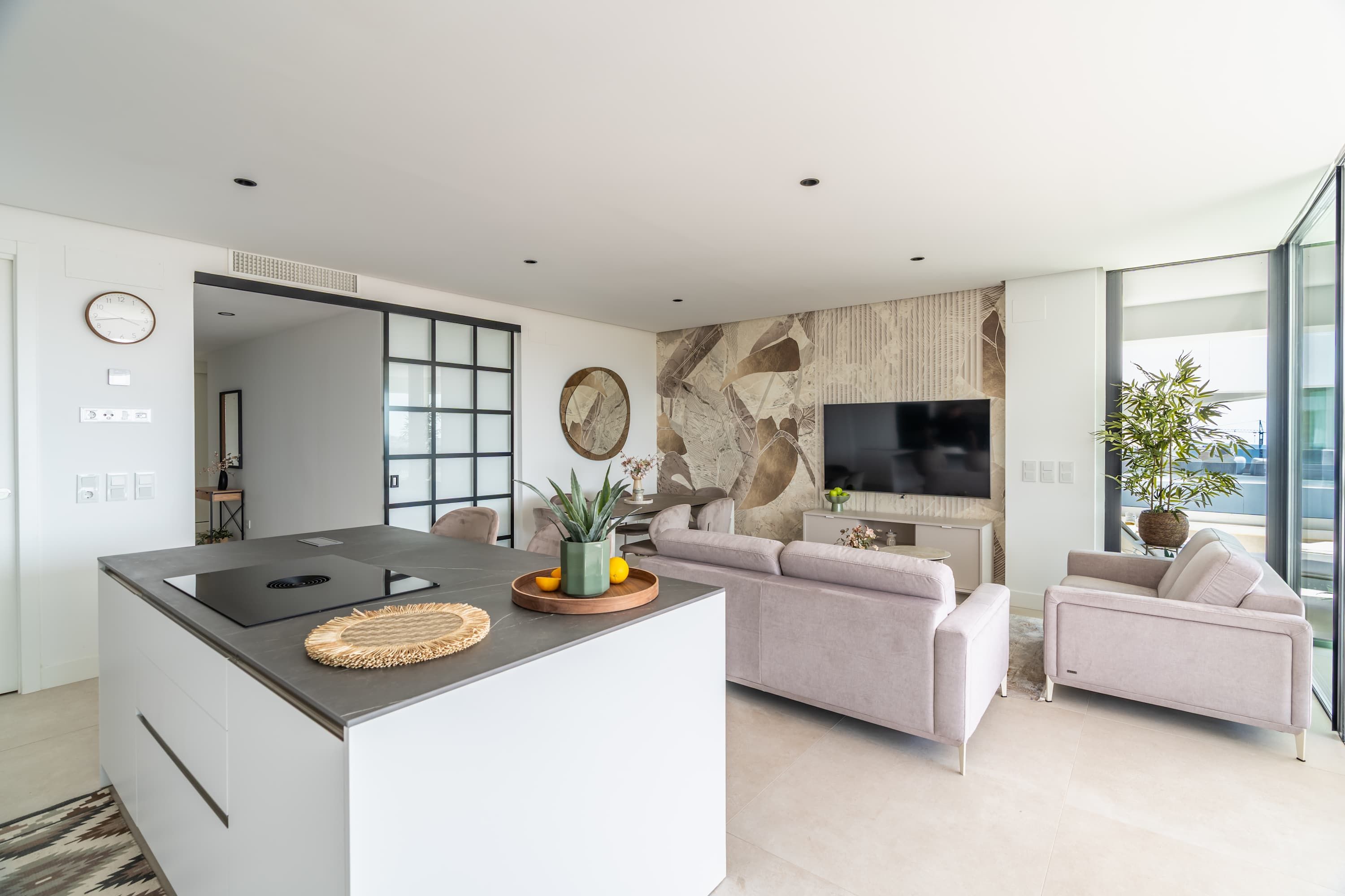 A modern living space with a kitchen island, sofa, and a flat-screen TV mounted on the wall.