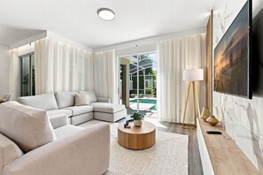 A modern living room with a sectional sofa, a round wooden coffee table, and a large TV mounted on the wall. - Chic Disney Retreat with Fun Themed Rooms (Four Corners)