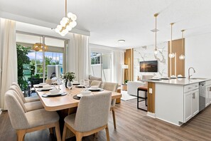 Una cocina moderna con salpicadero de mármol, comedor con mesa y sillas de madera, e iluminación colgante.