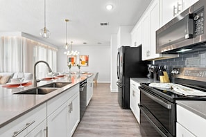 A modern kitchen with stainless steel appliances, a central island, and pendant lighting. - Themed Disney Getaway, Pool & Amazing Location (Four Corners)