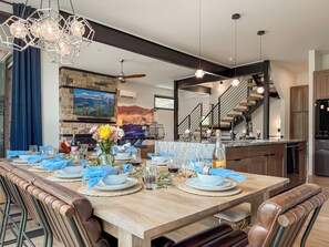 A dining area with a long wooden table set for a meal, a fireplace, and a staircase leading to an upper level. - Sleeps 18 | 2 Hot Tubs, Sauna & Game Room (Winter Park)