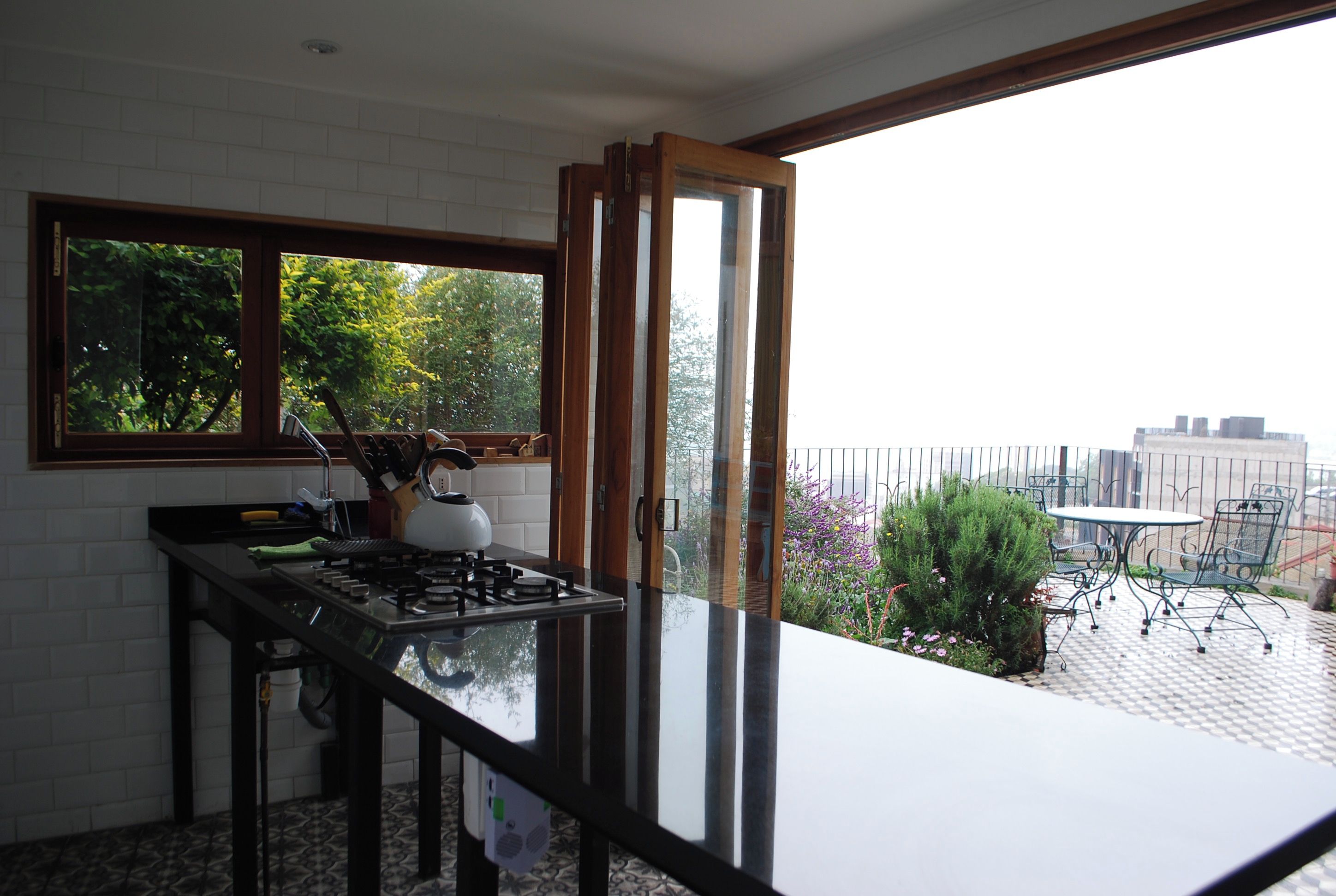 Een keuken met een gasfornuis, een raam en uitzicht op een balkon met buitenmeubilair.