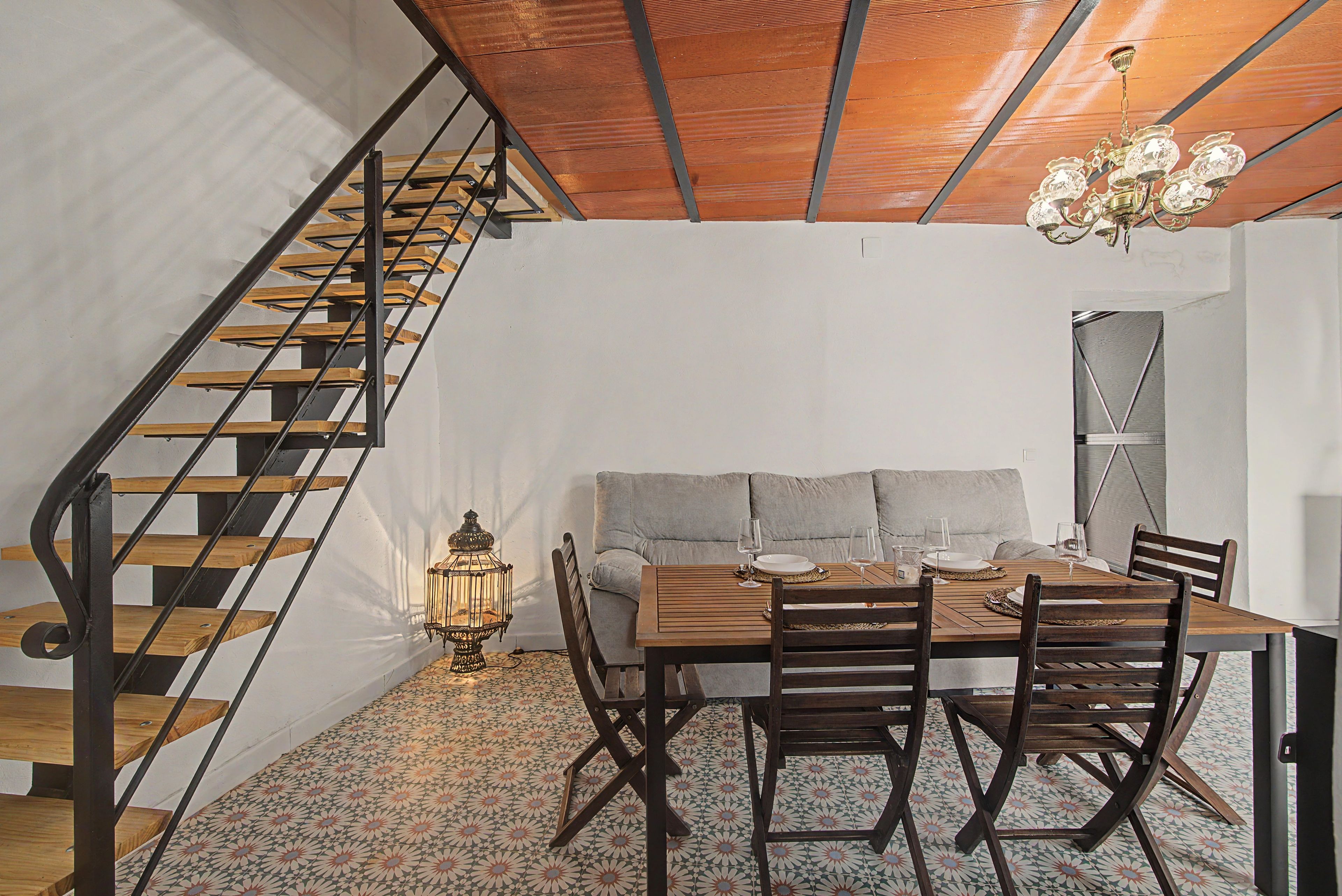 Un comedor con una mesa de madera, sillas y un sofá. Se ve una escalera con escalones de madera y barandillas de metal a la izquierda.