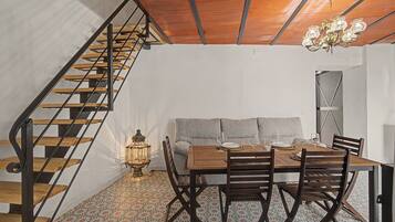 Un comedor con una mesa de madera, sillas y un sofá. Se ve una escalera con escalones de madera y barandillas de metal a la izquierda.