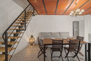 A dining area with a wooden table, chairs, and a sofa. A staircase with wooden steps and metal railings is visible to the left. - Vacation Home 'La Casa del Castillo' with Private Terrace, Wi-Fi & Air Conditioning (Niebla)