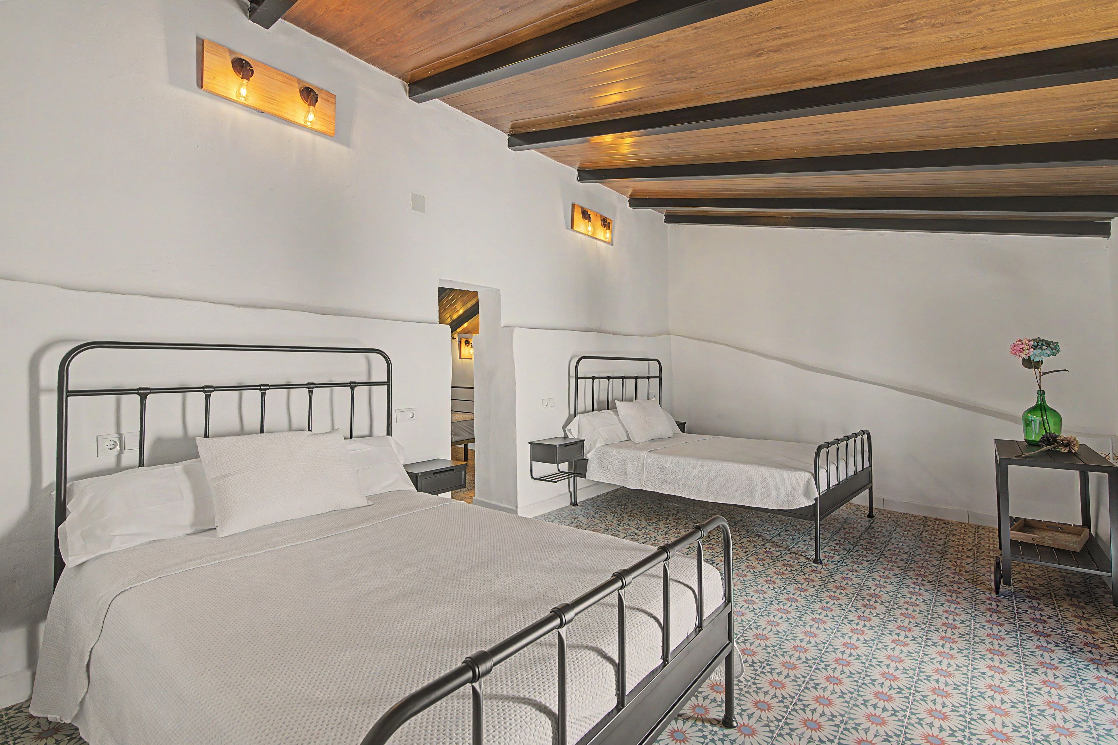 Een kamer met twee bedden, een klein tafeltje met een vaas en een kamer met een patroon vloer.
