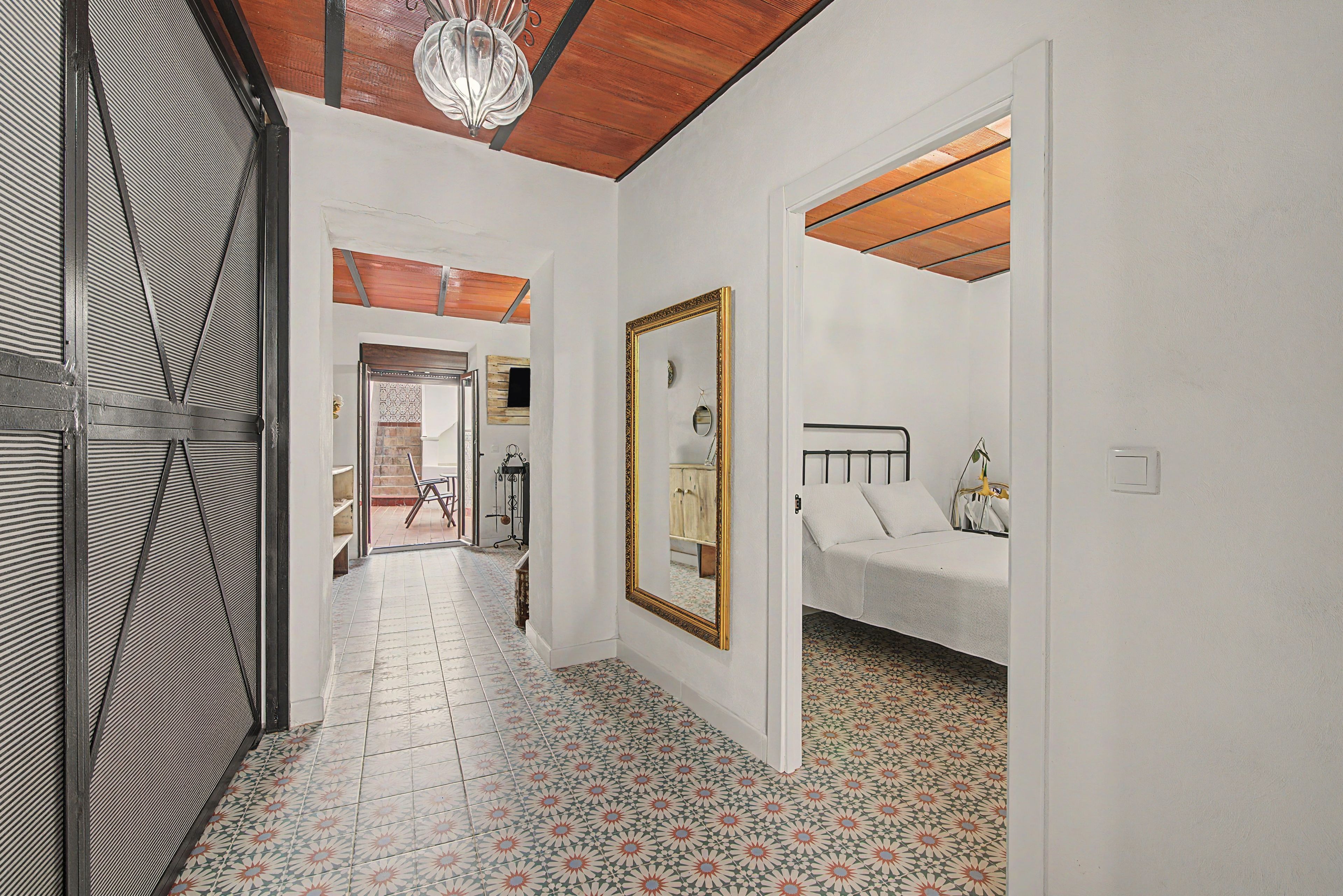 A hallway with a patterned floor, a bed with a headboard, a mirror, and a door leading to another room.