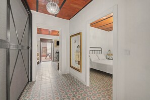 A hallway with a patterned floor, a bed with a headboard, a mirror, and a door leading to another room.