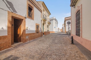 A cobblestone street flanked by buildings with traditional architecture, including wooden doors and barred windows.