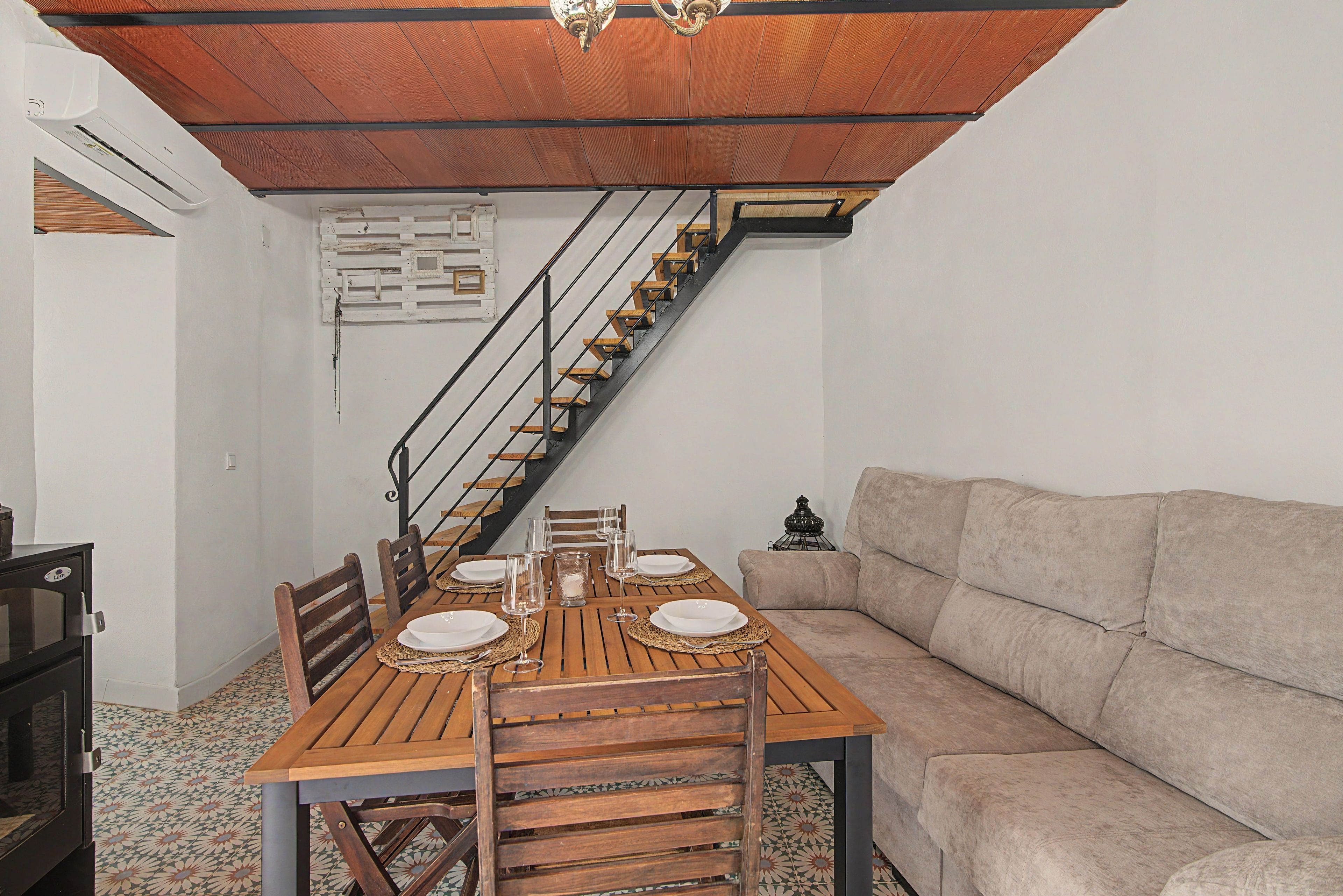 A dining area with a wooden table set for four, a sofa, and a staircase.