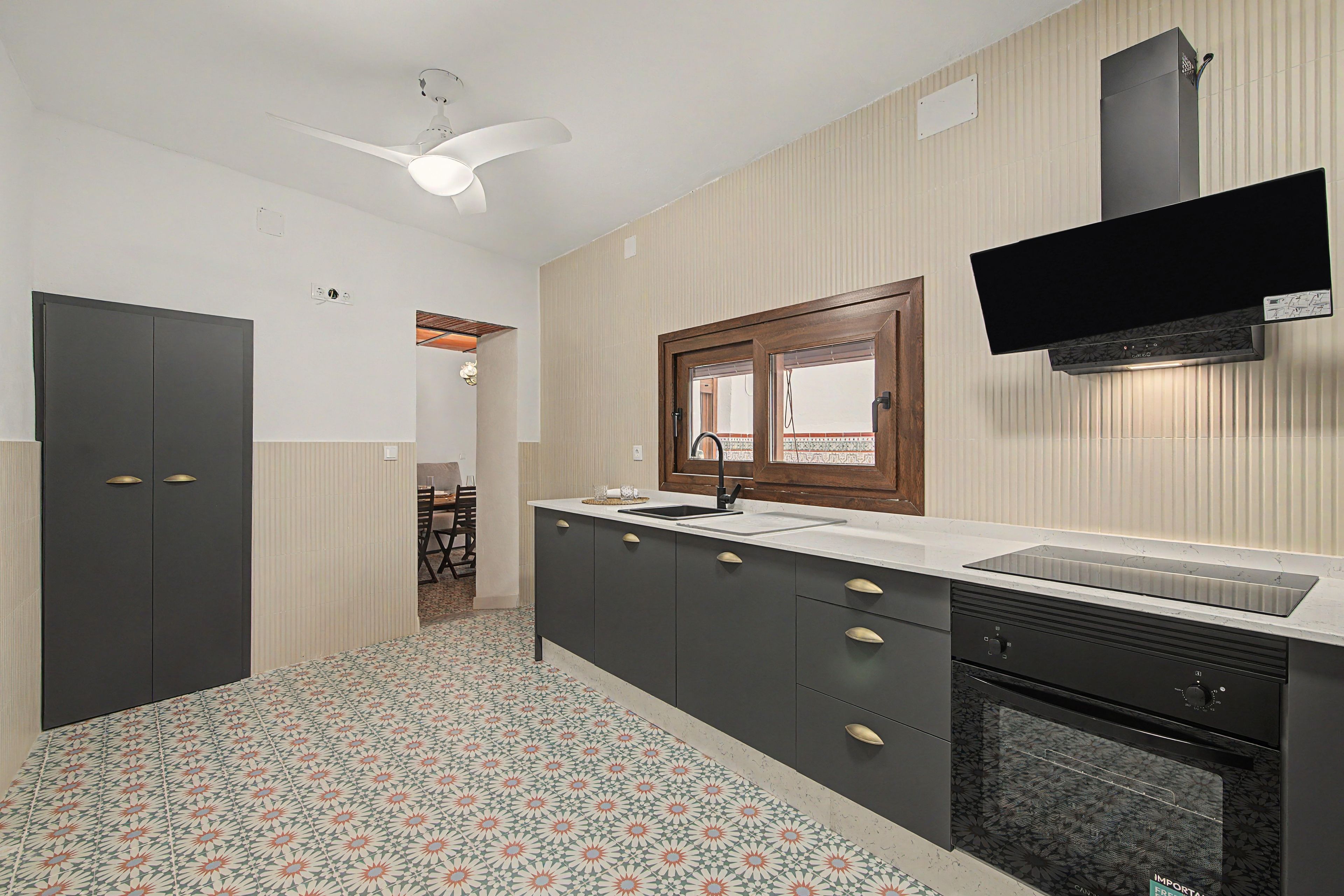 A modern kitchen with a built-in dishwasher, a window above the sink, and a ceiling fan.