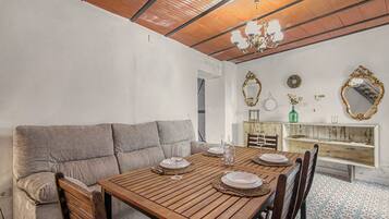 A dining area with a wooden table set for four, a grey sofa, and a wooden cabinet with decorative mirrors.