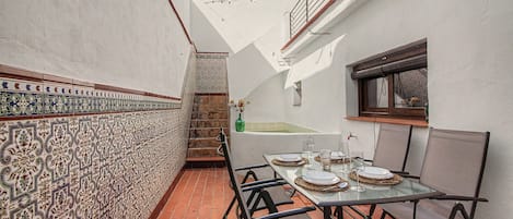Un comedor con una mesa lista para dos personas, una pared con azulejos y una escalera que sube a un nivel superior.