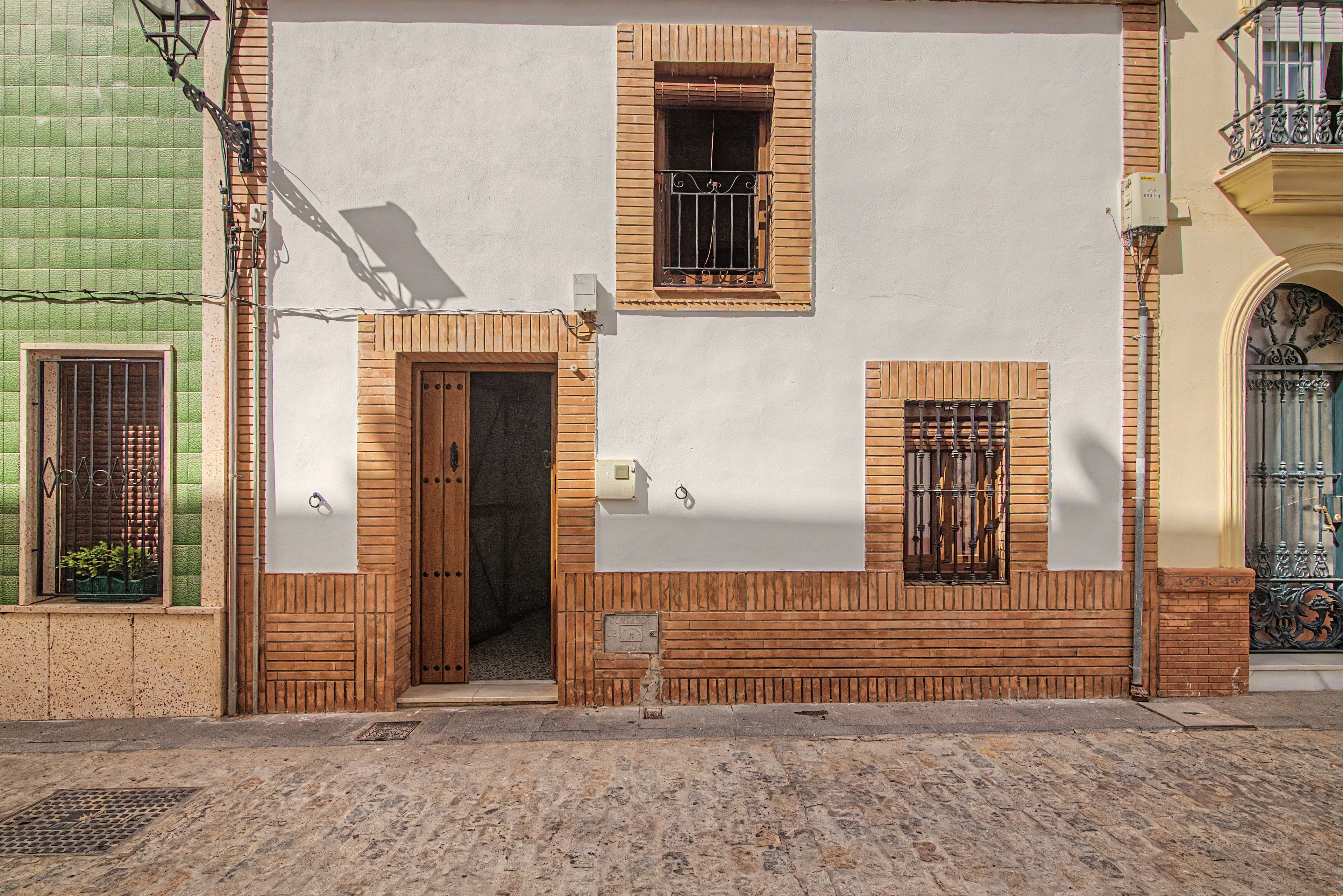 Un edificio con puerta de madera, una ventana con reja de metal y un pequeño balcón con barandilla metálica.