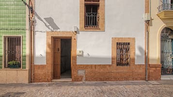 Un edificio con puerta de madera, una ventana con reja de metal y un pequeño balcón con barandilla metálica.