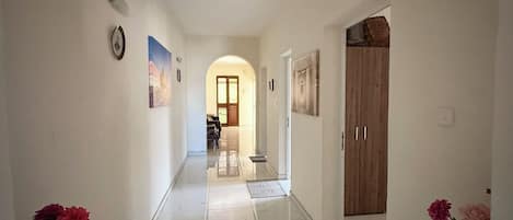 A hallway with a tiled floor, a wooden door, and a wall-mounted light fixture.