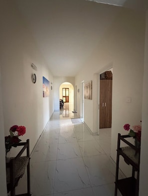 Un couloir doté d’un sol carrelé, d’une porte en bois et d’un luminaire fixé au mur.