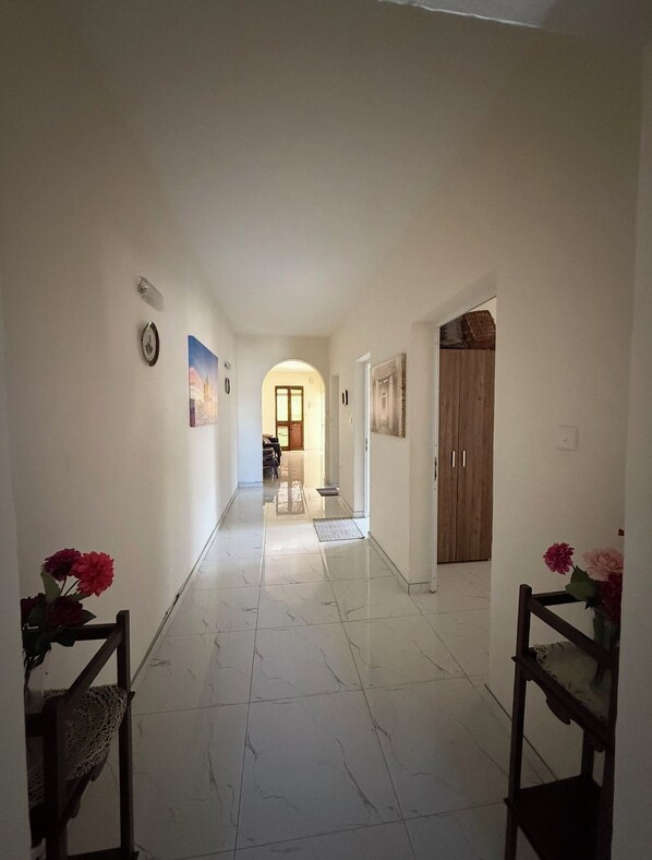 A hallway with a tiled floor, a wooden door, and a wall-mounted light fixture.