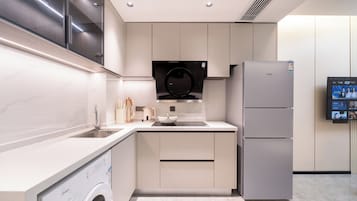 A modern kitchen with a built-in washing machine, a refrigerator, and a wall-mounted TV.