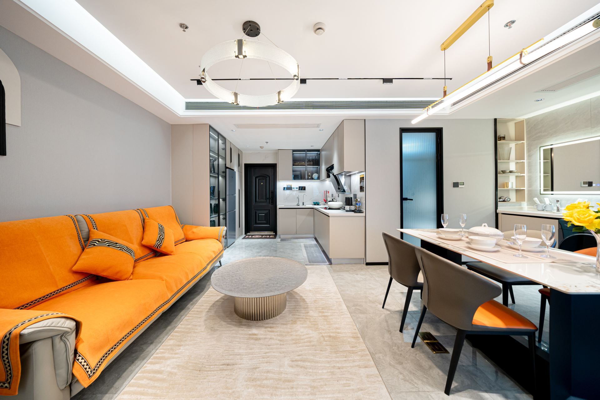 A modern living room with a sofa, a dining table set for two, and a kitchen in the background.
