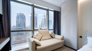 A modern hotel room with a sofa, a bed, and a large window offering a city view. - Shijia Homestay - Shanghai Century (Shanghai)