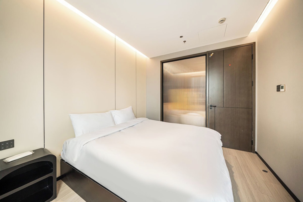 A modern hotel room with a bed, a wardrobe, and a bedside table.