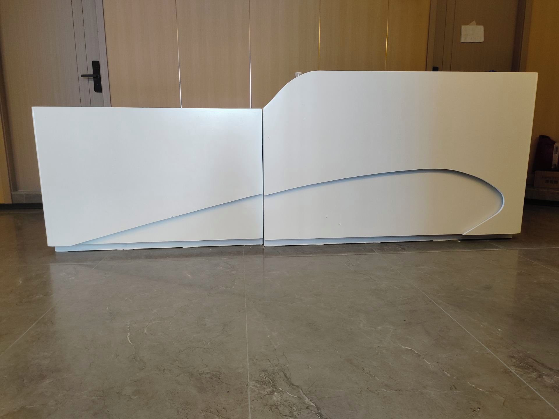 A reception desk with a curved design, positioned in a room with a wooden door and a tiled floor.