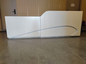 A reception desk with a curved design, positioned in a room with a wooden door and a tiled floor.