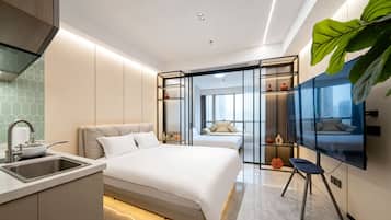 A modern hotel room with a bed, a TV, a desk with a sink, and a large window.