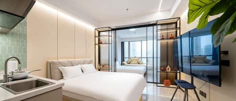 A modern hotel room with a bed, a TV, a desk with a sink, and a large window.
