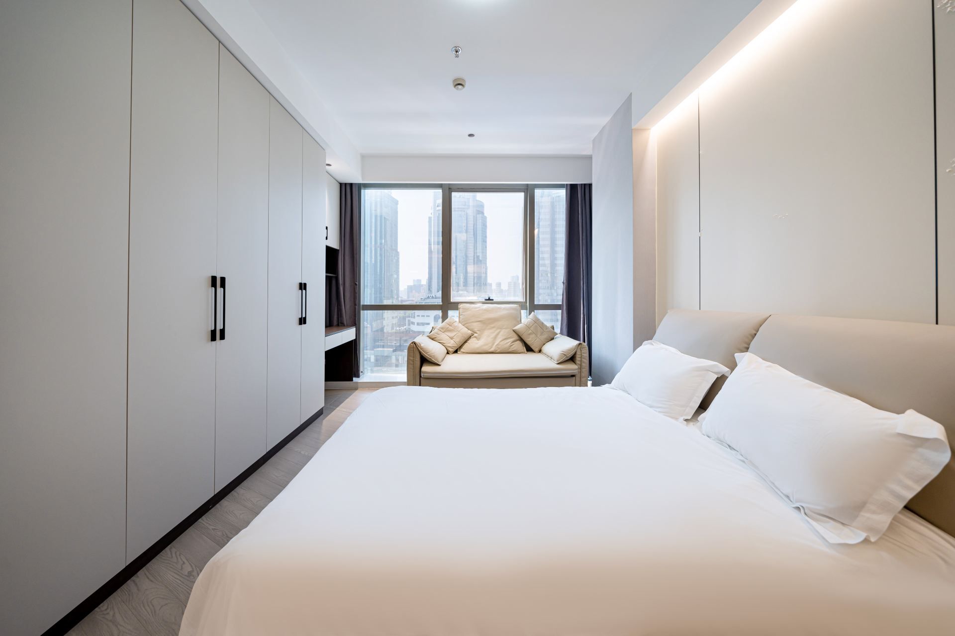 A modern hotel room with a large bed, a sofa, and a city view.