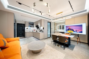 A modern hotel room with a dining area, a TV, and a kitchen.